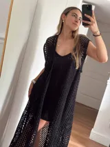 Chaleco largo sin mangas, tejido en punto calado tipo red con hilo de algodón y lurex, color marrón. Presenta escote profundo en V, tiras para atar en el frente, tajo trasero y flecos en el ruedo.