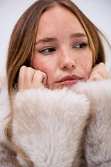 Campera de piel sintética en tono beige con textura suave y voluminosa. Presenta cuello alto, cierre frontal completo y mangas largas con puños amplios.