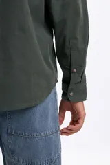 Camisa de manga larga confeccionada en micropana color verde militar, con cuello abotonado, bolsillo frontal y cierre de botones.