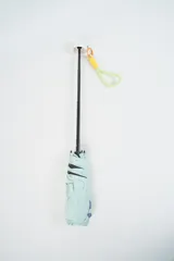 Paraguas plegable de color beige con la palabra 'hello.' estampada en color verde. Incluye una correa de muñeca de color amarillo con detalles en fucsia.