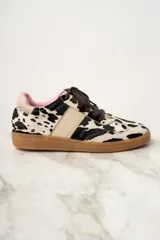 Zapatillas bajas de cuero con estampado de vaca en blanco y negro, cordones marrones y suela de goma color caramelo.