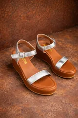 Sandalias de plataforma con tiras de cuero metalizado color dorado y base de plataforma color marrón. Cierre con hebilla ajustable en el tobillo.