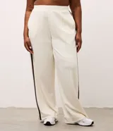 Pantalón deportivo de corte oversized estilo college, confeccionado en microfibra color crema con rayas laterales contrastantes en color marrón. Presenta cintura fija, bolsillos funcionales y frisos frontales.