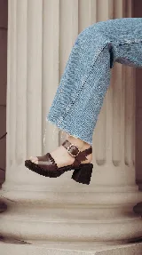 Sandalia Bruna de cuero y gamuza en tonos marrones y beige, con taco ancho, plataforma y tira al tobillo con hebilla metálica.