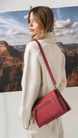 Bandolera de tamaño mediano en color gris, confeccionada en símil cuero con textura granulada. Presenta un bolsillo frontal con cierre, herrajes metálicos oscuros y correa ajustable y desmontable.
