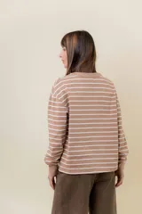 Buzo liviano de manga larga con diseño de rayas horizontales en color beige y blanco. Presenta un cuello redondo con cartera frontal de botones tipo henley, hombros caídos y calce holgado con puños acanalados.