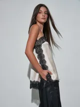 Musculosa de satén color beige claro, con detalles de encaje negro en el escote, los laterales y el ruedo, y tirantes finos.