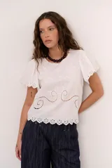 Blusa blanca de manga corta con detalles de bordados y perforaciones, cuello redondo y diseño holgado.