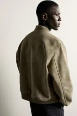 Campera bomber color verde militar de corte relaxed fit, confeccionada en tejido efecto ante, con cuello, puños y dobladillo en rib elástico, bolsillos frontales de vivo y cierre central con cremallera.