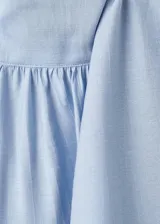 Blusa de color celeste con cuello alto y detalle de fular integrado para anudar. Presenta mangas largas con puños abotonados y un diseño de corte recto.