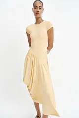 Vestido largo color amarillo pastel, confeccionado con mezcla de viscosa, con cuello redondo, manga corta y bajo asimétrico fruncido con volumen.