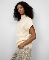 Chaleco de punto color crema, con cuello chimenea y diseño de ochos trenzados. Presenta mangas sisa con hombro caído.