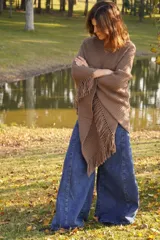 Poncho tejido en lana merino color marrón, con diseño de punto acanalado y terminación con flecos en el borde inferior. Incluye una pequeña etiqueta de cuero en la parte posterior.