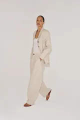 Pantalón barrel de tiro medio confeccionado en hilatura con lino, color beige con diseño a rayas sutiles. Cuenta con cintura con trabillas, bolsillos laterales ocultos en costura, pierna ancha y cierre frontal con cremallera y botón.