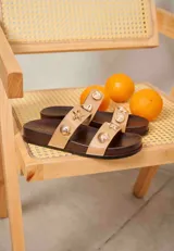 Sandalias planas con base de madera oscura y dos tiras en el empeine de color tostado, decoradas con apliques metálicos dorados en forma de conchas marinas y estrellas de mar.