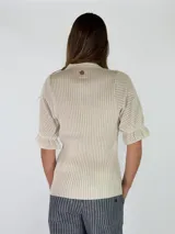 Top de tejido de punto color terracota, con escote en V, cuello camisero y cartera frontal con botones. Presenta mangas cortas con textura calada y puños con volados.