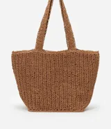 Bolso de playa tejido en fibra de papel color marrón claro, con asas medianas y detalle de logo metálico dorado en el centro.