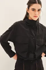 Campera negra de estilo militar o utilitario, con cuello alto, bolsillos delanteros con tapa y cordón ajustable en el ruedo.