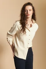 Camisa de pana color crema con cuello camisero con volados, cierre frontal de botones y mangas largas con puños abotonados. Presenta un bolsillo aplicado en el pecho y una silueta relajada.
