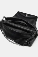 Bolso bandolera de hombro en color negro, con diseño de costuras horizontales y verticales. Cuenta con una cadena metálica plateada que funciona como correa y un asa de mano superior. El cierre es mediante botón imantado.