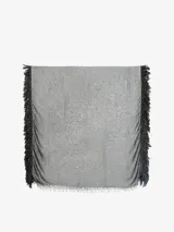 Pañuelo fino de tejido ligero, color gris, con flecos largos y densos en los bordes laterales y flecos más cortos en los bordes superiores e inferiores.