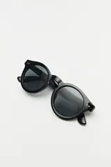 Lentes de sol con marco redondeado de color negro y cristales oscuros. Presentan un diseño clásico con detalles metálicos sutiles en las esquinas del frente.