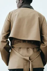 Gabardina corta de sarga color marrón claro, con doble botonadura, cuello de solapa en contraste de color negro con efecto cuero, bolsillos laterales con solapa y cinturón ajustable para anudar en la cintura.