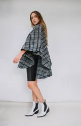 Poncho de paño con estampa a cuadros en tonos grises, negros y blancos, con cuello camisero gris y cierre frontal con dos botones.