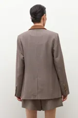 Blazer de corte sastre con estampado de cuadros pequeños en tonos tierra. Presenta solapas y detalles en los bolsillos de gamuza en color marrón, cierre frontal de doble botonadura y estructura entallada.
