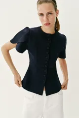 Chaqueta entallada azul marino de punto, con cuello redondo y mangas cortas abullonadas con aberturas. Cierre frontal con botones forrados a tono.