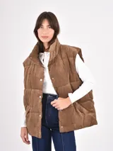 Chaleco acolchado de pana color marrón, diseño puffer sin mangas con cuello alto y cierre frontal de botones a presión.