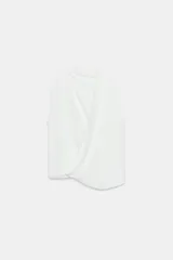 Top blanco de manga sisa con cuello redondo y diseño drapeado cruzado en la parte frontal, con bajo asimétrico y cierre en la espalda con abertura y botones.