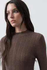 Polera de tejido de punto con textura calada y diseño de líneas verticales acanaladas. Presenta cuello alto y mangas largas con puños delicados, de silueta entallada.