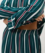 Pijama de dos piezas estilo americano confeccionado en viscosa. Incluye una camisa de mangas largas con cuello solapa, cierre frontal con botones y detalle de vivo contrastante, junto con un pantalón de cintura elástica. Presenta un diseño estampado a rayas verticales en tonos verde, blanco y bordó.