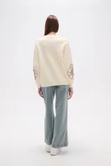 Sweater de tejido de punto color crema, con diseño holgado, cuello redondo a la base y mangas largas. Presenta apliques bordados en relieve con forma de flores en tonos rosados en el frente y las mangas.