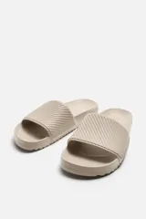 Chancla tipo pala monocolor negra, con suela de goma y tira ancha en el empeine con relieve acanalado.