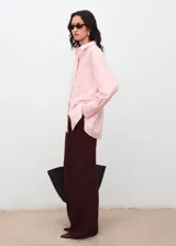 Camisa oversize color rosado, con cuello camisero, manga larga con puños abotonados, bolsillo de parche en el pecho y cierre frontal con botones ocultos.