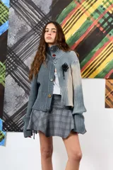 Saco de hilo con cuello alto y cierre de botones, de tejido de punto y diseño oversize. Presenta un teñido artesanal degradado que combina gris y beige, con mangas largas y puños amplios, además de un detalle de aplicación floral oscura en el pecho.