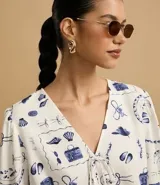 Blusa de mangas abullonadas cortas, confeccionada en Viscolino con 15% de Lino, con cuello v con lazo y estampa de accesorios de playa.