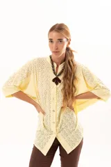 Camisa de corte oversize y mangas murciélago, confeccionada en tela con perforaciones tipo broderie. Presenta cuello mao, cierre frontal con botones y un diseño holgado y fluido.