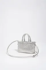Minibolso estructurado de cuero trenzado color plateado, con asas de mano y correa larga de hombro ajustable. Incluye una pequeña etiqueta de cuero con logotipo grabado en la parte frontal.