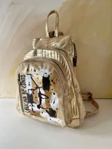 Mochila de cuero de Carolina De Cunto, modelo Lucy Natu Gold Arte. Presenta combinación de tonos naturales y dorados con textura efecto cocodrilo, diseño frontal intervenido con arte pintado a mano y bolsillo vertical con cierre.