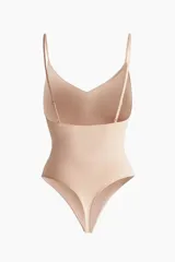 Body modelador tipo tanga color beige, con efecto vientre plano. Presenta copas forradas con sección en punto menguado para realce y sujeción suave, sin aros. Cuenta con breteles ajustables y cierre inferior con botones a presión ocultos. Diseño sin costuras para mayor comodidad.
