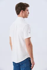 Camisa de manga corta confeccionada en tejido piqué de algodón, color blanco, con cuello con botones y cierre frontal abotonado.