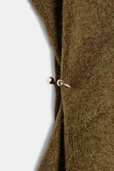 Top de punto color verde militar, con cuello subido y manga sisa. Presenta apliques dorados en los laterales y un bajo asimétrico.