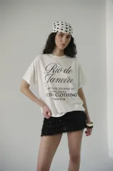 Remera de algodón blanca con estampado frontal en negro que dice "Rio de Janeiro" en letra cursiva y "Captivate Journey to Copacabana Lucha Clothing since 2019".