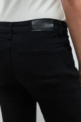 Pantalón de denim negro, corte slim, con cintura media y cierre frontal con botón y cremallera.