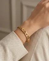 Esclava de acero con baño de oro, con diseño de eslabones tipo cadena en la parte superior y una cadena fina adicional integrada.