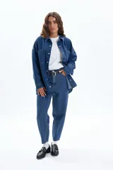Sobrecamisa de jean color azul oscuro, con corte oversize, cuello clásico, cierre frontal con botones metálicos y dos bolsillos frontales tipo parche.