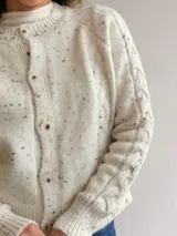 Cárdigan de punto gris con efecto jaspeado, diseño de trenzas en las mangas, cuello redondo y cierre frontal con botones. Presenta puños y ruedo acanalados.